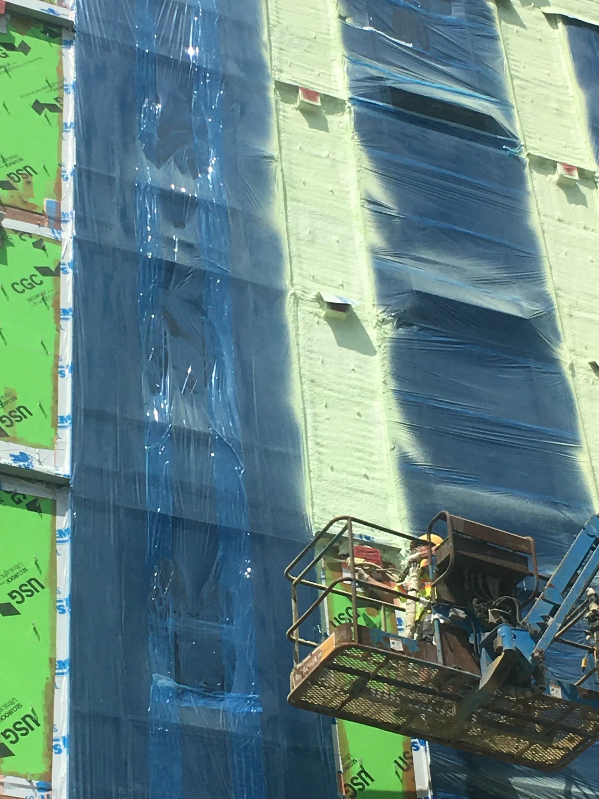 Crew on a lift detailing a green and blue air barrier on a multi-storey wall