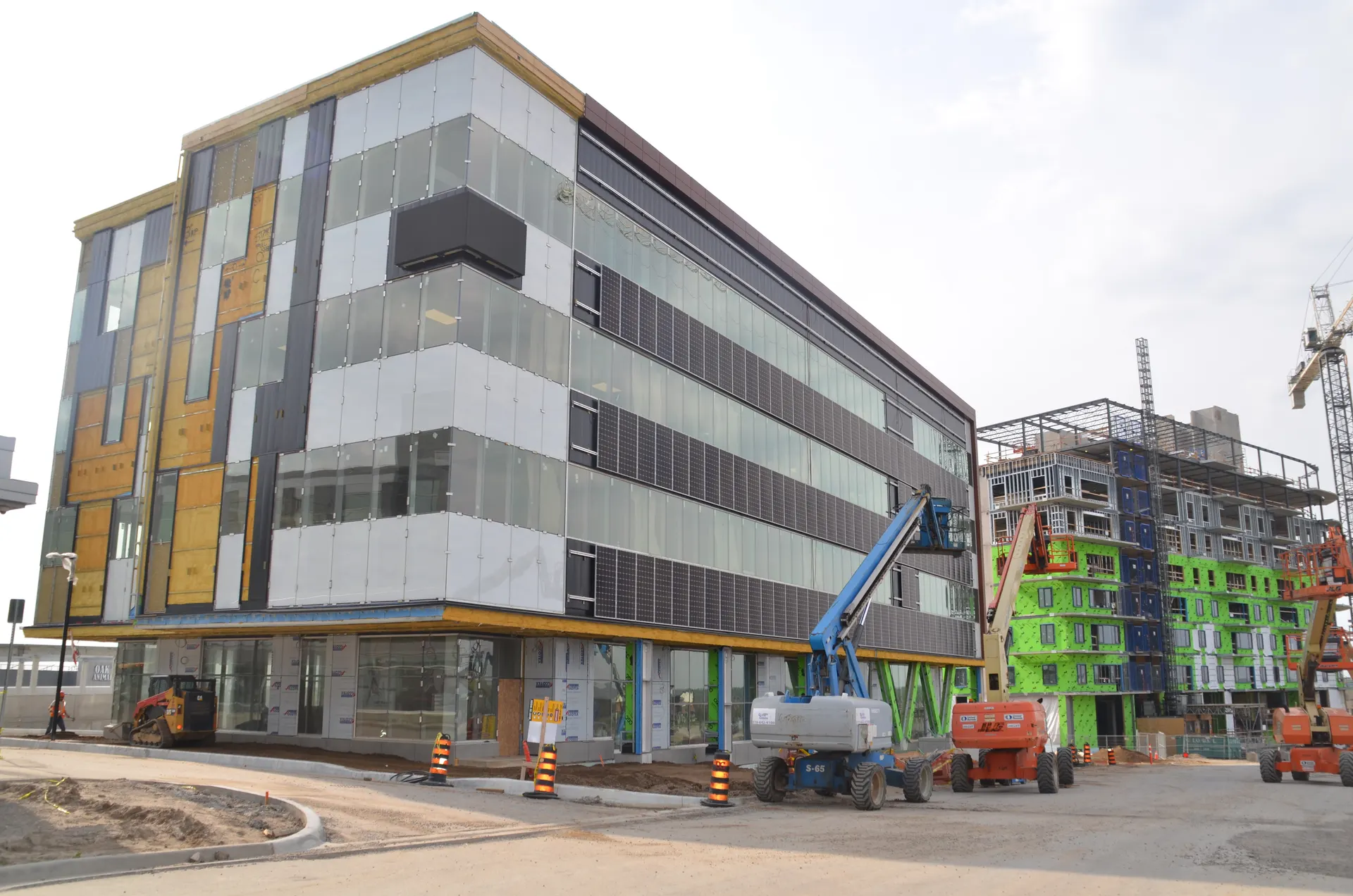 Completed mid-rise envelope beside a building wrapped in green barrier