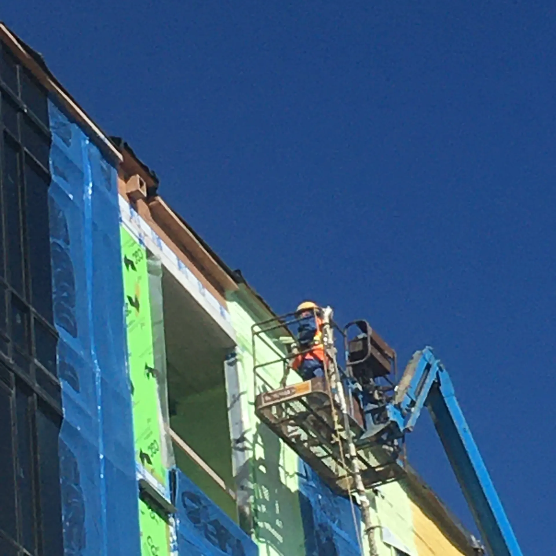Applicator on a lift detailing a blue air barrier on a mid-rise exterior