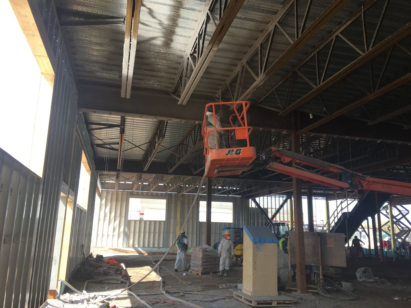 Spray-applied fireproofing crew under an open steel deck